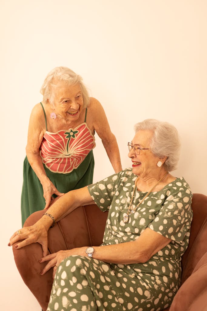 Two senior women in cheerful conversation indoors, exuding warmth and friendship.